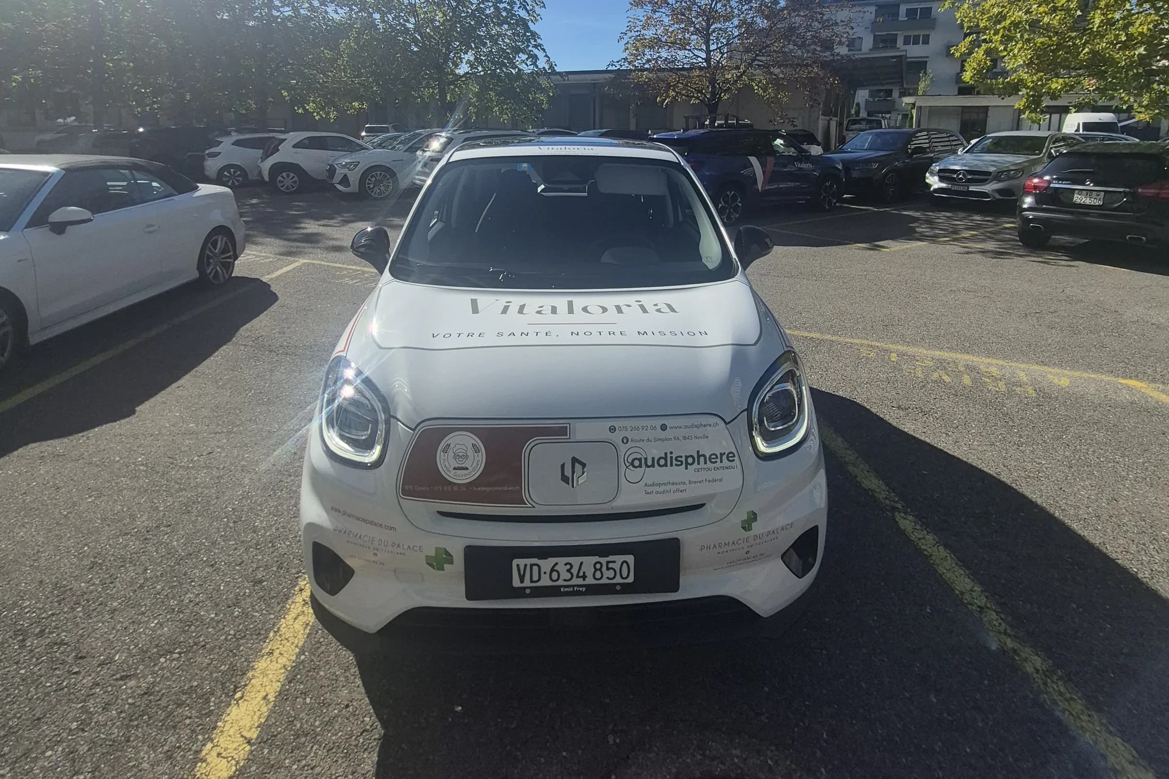 L'avant de la nouvelle voiture Vitaloria, blanche, avec le nom et le slogan « Votre santé, notre mission » sur le capot
